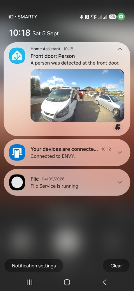 A Home Assistant phone notification reading 'Front door: Person — A person was detected at the front door', with the daytime snapshot of a person walking up the driveway between the parked cars